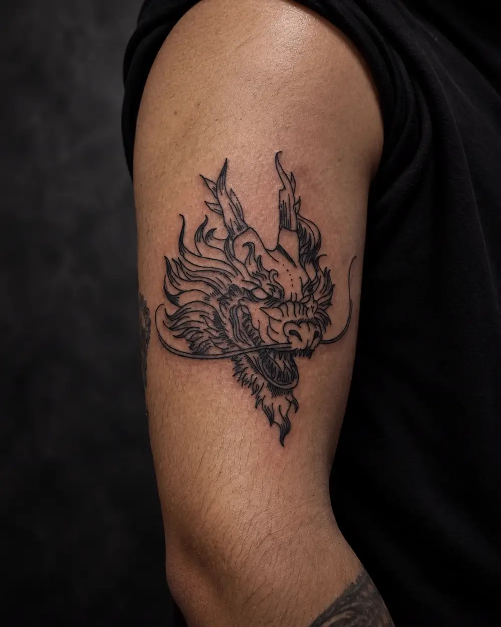 Tatuaje fine line de cabeza de dragón japonés en el bíceps por Lucca Haro, tatuador en Buenos Aires (CABA)